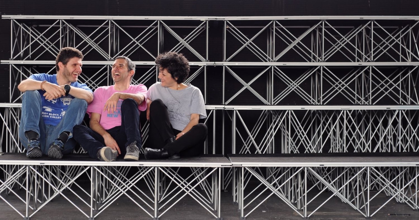 Εικόνα Playground for the Arts Α.Μ.Κ.Ε. που απεικονίζει τρεις ανθρώπους να συζητούν γελώντας, καθισμένοι σε μία κερκίδα.