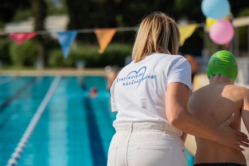 Εικόνα με ένα παιδί με αναπηρία που λαμβάνει υποστήριξη στην πισίνα.