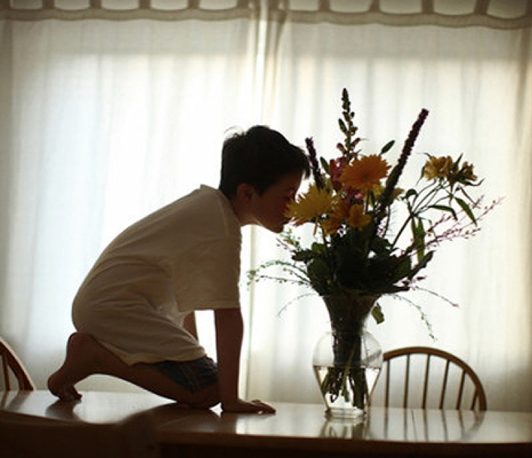 Εικόνα παιδιού με αυτισμό πάνω στο τραπέζι, μυρίζει τα λουλούδια.
