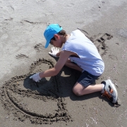 Εικόνα που παρουσιάζει ένα παιδί να σχηματίζει μία καρδιά στην άμμο.